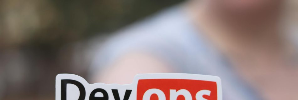 A close-up image featuring a DevOps sticker held by a person outdoors.