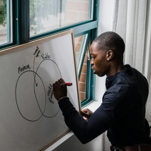 African American man writing on whiteboard with Venn diagram, indoors.