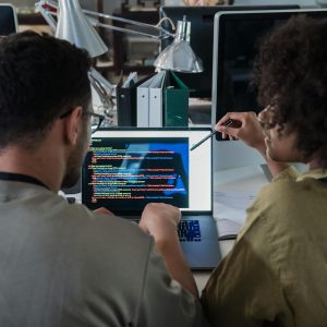 Two developers engage in software programming on a laptop in a modern office setting.