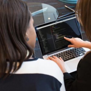 Two women working together on software programming indoors, focusing on code.