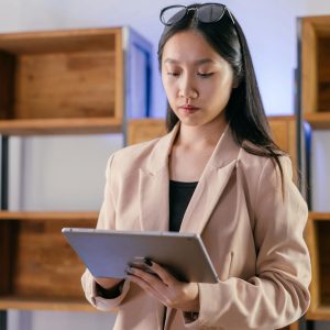 Young Asian businesswoman using a tablet in a modern office setting.